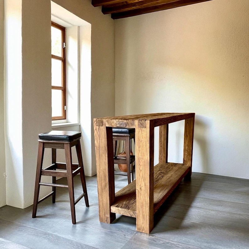 Peut inclure: Une console en bois massif avec une &eacute;tag&egrave;re inf&eacute;rieure et un tabouret de bar assorti avec une assise en cuir noir. La table est en bois brun clair et de forme rectangulaire. Le tabouret est brun fonc&eacute;.