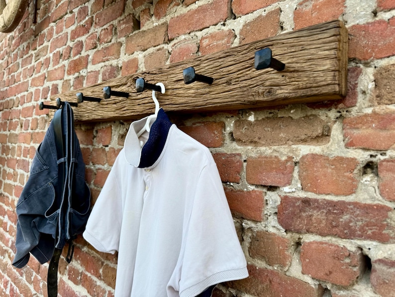 May include: A rustic wooden coat rack with black metal hooks. The rack is mounted on a brick wall and has a white shirt and blue jeans hanging from it.