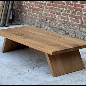 Puede incluir: Mesa de centro rectangular de madera con acabado natural. La mesa tiene un dise&ntilde;o sencillo y moderno con patas anguladas. La veta de la madera es visible y la mesa est&aacute; colocada contra una pared de ladrillo.