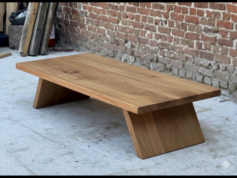Puede incluir: Mesa de centro rectangular de madera con acabado natural. La mesa tiene un dise&ntilde;o sencillo y moderno con patas anguladas. La veta de la madera es visible y la mesa est&aacute; colocada contra una pared de ladrillo.
