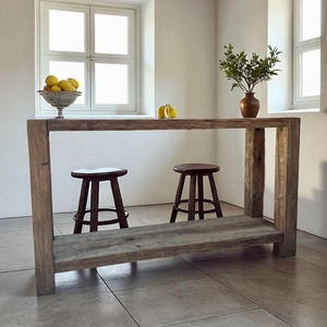 Peut inclure: &Icirc;lot de cuisine en bois rustique avec une &eacute;tag&egrave;re inf&eacute;rieure et deux tabourets marron fonc&eacute;. La surface de l'&icirc;lot contient un bol de citrons, un vase avec de la verdure et deux citrons. La pi&egrave;ce a des murs et des fen&ecirc;tres blancs.