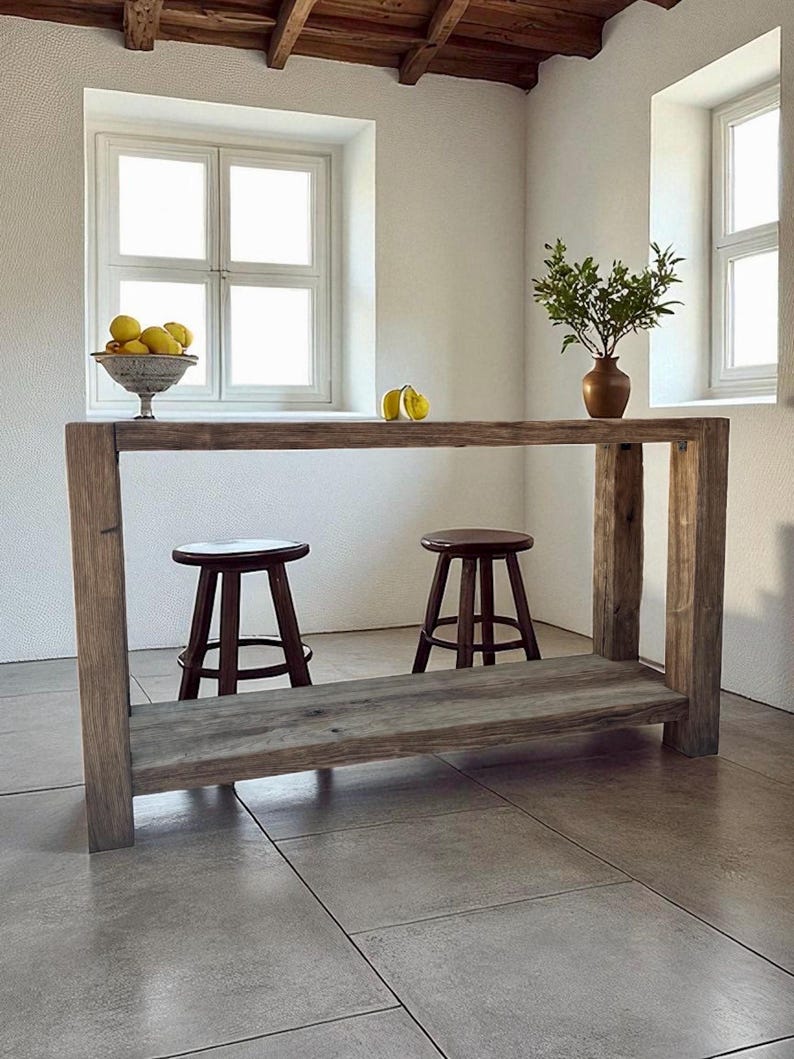 Peut inclure: &Icirc;lot de cuisine en bois rustique avec une &eacute;tag&egrave;re inf&eacute;rieure et deux tabourets marron fonc&eacute;. La surface de l'&icirc;lot contient un bol de citrons, un vase avec de la verdure et deux citrons. La pi&egrave;ce a des murs et des fen&ecirc;tres blancs.