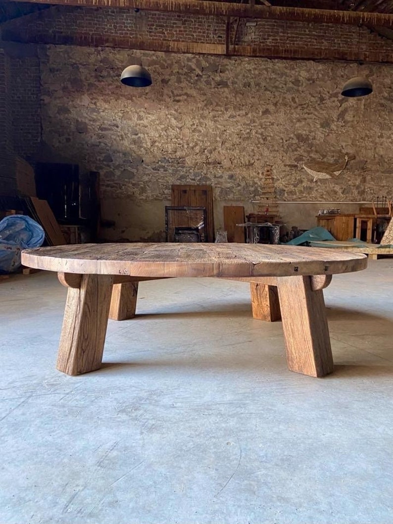 May include: A large, round wooden table with a rustic finish and four thick, sturdy legs. The table is made of reclaimed wood and has a natural, weathered look.
