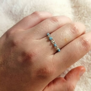 Puede incluir: Un anillo de plata con una fila de cuentas de color azul claro.