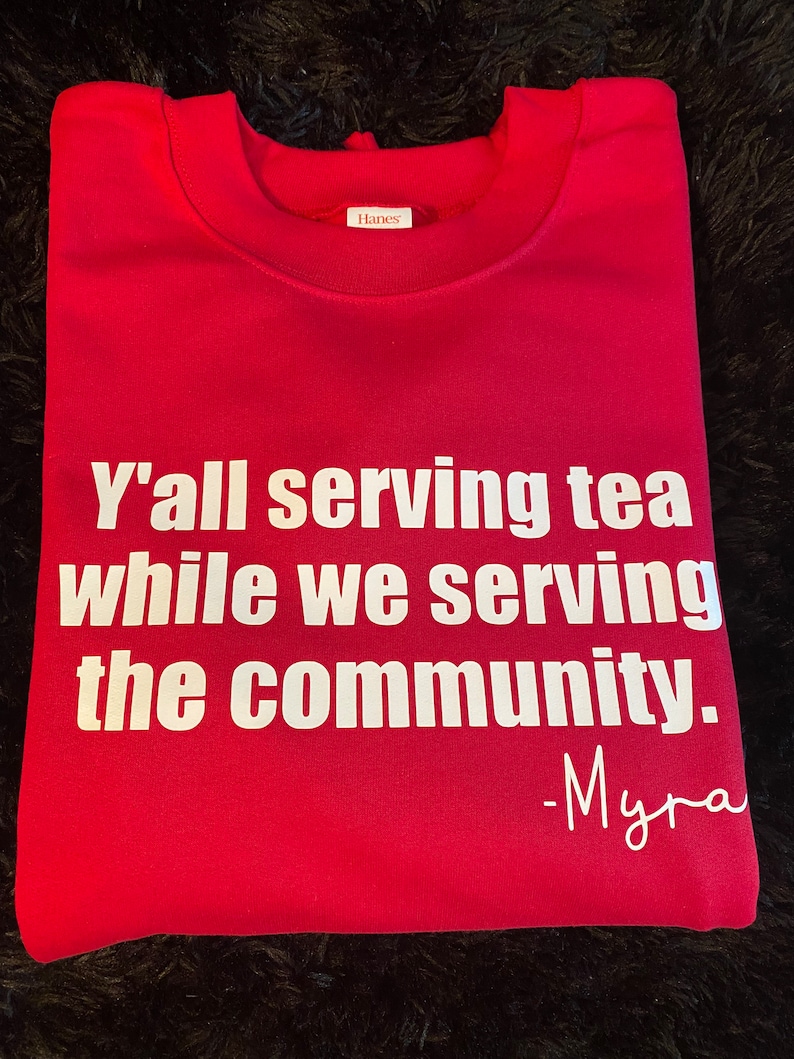 May include: Red sweatshirt with white text that reads "Y'all serving tea while we serving the community. -Myra"