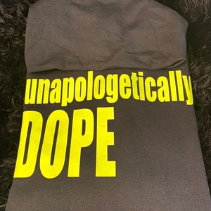 May include: Black hooded sweatshirt with the words "unapologetically DOPE" printed in yellow.