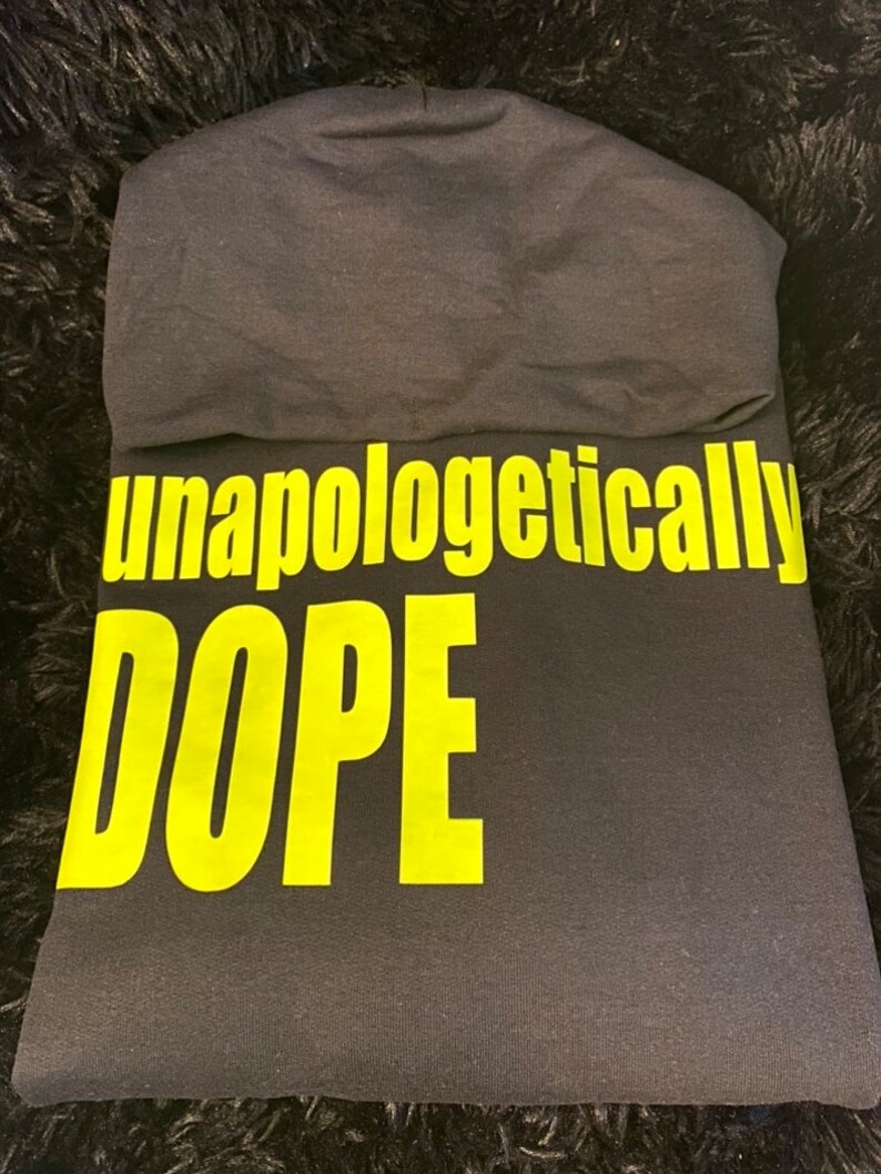 May include: Black hooded sweatshirt with the words "unapologetically DOPE" printed in yellow.