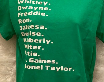 Op de afbeelding: Een groen t-shirt met witte tekst met namen: Whitley, Dwayne, Freddie, Ron, Jaleesa, Delise, Kimberly, Witer, tie, Gaines en lonel Taylor. Het shirt is gemaakt van een zacht materiaal.