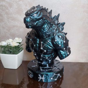 May include: A dark teal and black monster bust featuring a textured, scaly surface with silver-painted constellation patterns across the chest and back. The circular base displays silver zodiac symbols, including the Cancer and Pisces signs.
