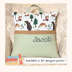 May include: A square reading pillow with a top section featuring a forest animal print with bears, deer, and foxes on a white background. The bottom section is light green with a dotted pattern and the embroidered name Jacob in dark green thread.