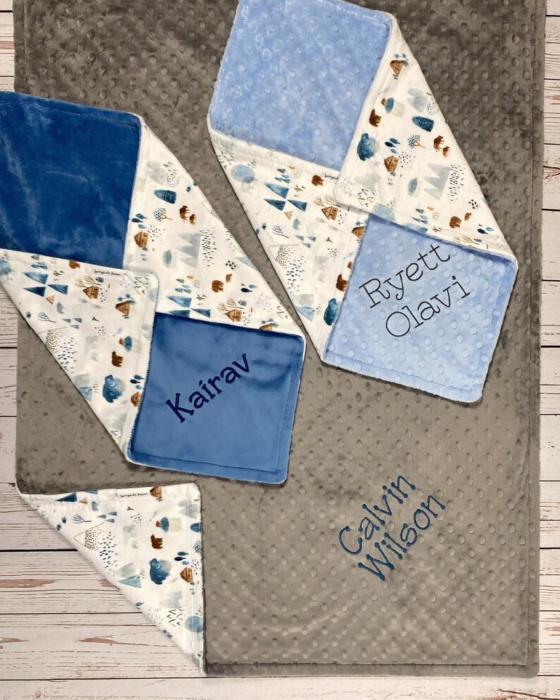May include: Four personalized baby blankets with a gray, white, and blue color scheme. The blankets feature a woodland design with trees, mountains, and bears. The names "Kairav", "Ryett Olavi", "Calvin Wilson", and "Kairav" are embroidered on the blankets.