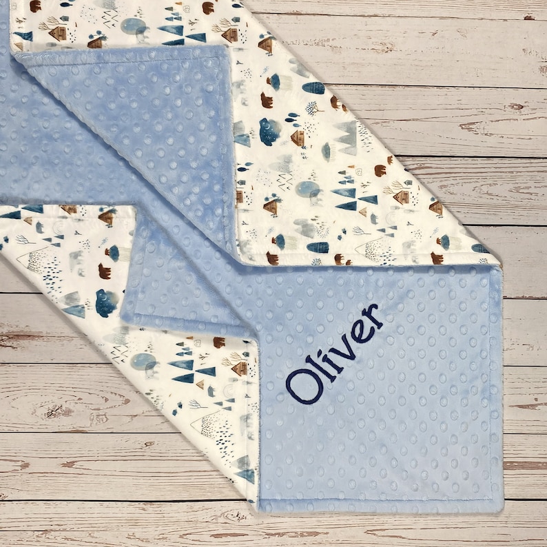 May include: A blue and white baby blanket with a woodland pattern and the name "Oliver" embroidered on it.