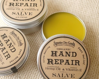 May include: Two open containers of organic hand repair salve with a yellow salve inside. The labels are brown with white text that reads "Superior Dry Goods", "Organic", "Hand Repair", "Cold-Pressed Hemp Oil & Vitamin E", "Salve", and "Fast Relief". One container is 4 oz. (120 ml) and the other is 2 oz. (60 ml).