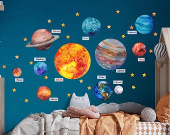 May include: A blue wall with a solar system wall decal featuring planets, stars, and the names of each planet in German. The planets are painted in watercolor style and include Pluto, Saturn, Uranus, Neptune, Jupiter, Mars, Venus, Earth, Mercury, and the Sun.