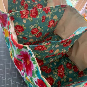 May include: A three-section fabric storage bin with a floral print featuring red, pink, and yellow flowers on a teal background. The bin is made of a soft, durable fabric and has a cream-colored lining.