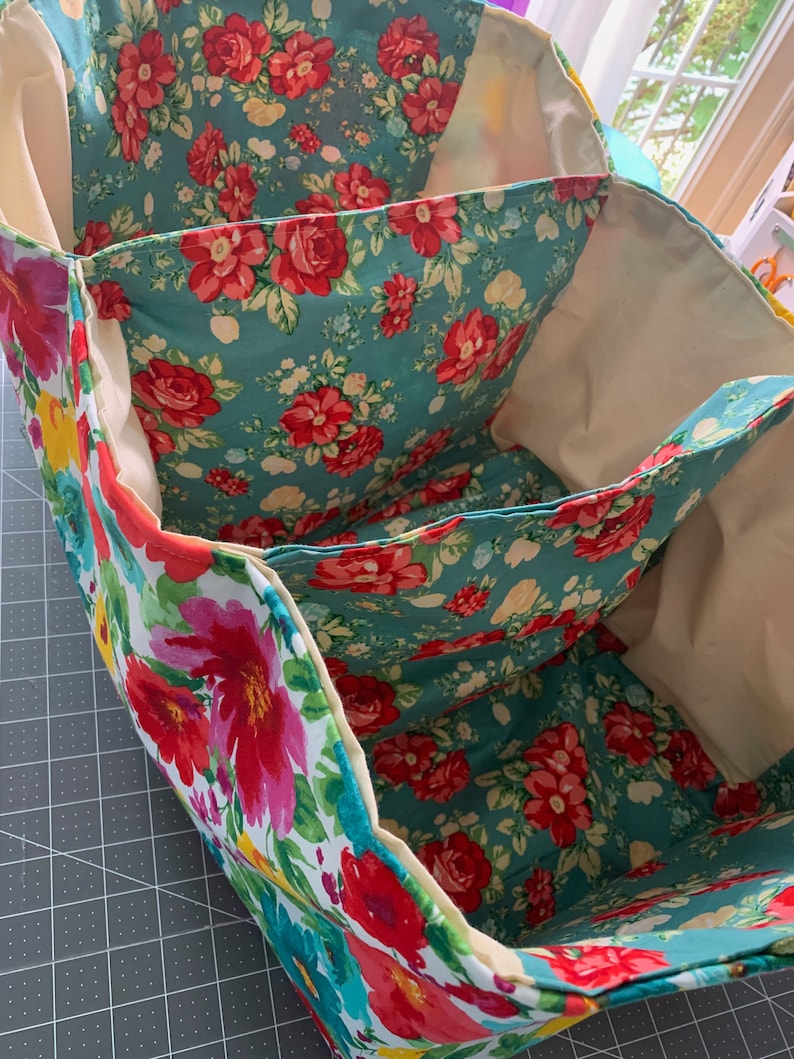 May include: A three-section fabric storage bin with a floral print featuring red, pink, and yellow flowers on a teal background. The bin is made of a soft, durable fabric and has a cream-colored lining.