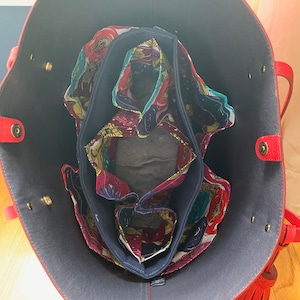 Op de afbeelding: De binnenkant van een rode tote bag met een donkerblauwe voering. De tas is gevoerd met een bloemenstof in tinten rood, geel, groen en blauw.