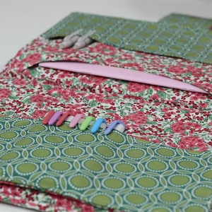 Könnte beinhalten: Stoff-Organizer mit rosa Innentasche und grünem geometrischen Rand. Das Gewebe hat ein rotes Blumenmuster. Mehrere farbige Häkelnadeln sind sichtbar. Ideal für Handarbeitszubehör.