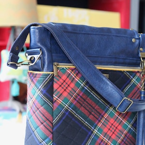 May include: A blue leather shoulder bag with a plaid fabric lining. The bag has a zippered pocket and a long adjustable strap.
