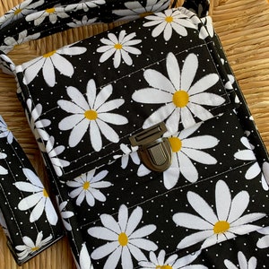 May include: A black crossbody bag with a white daisy print and white polka dots. The bag has a silver clasp and a black adjustable strap.