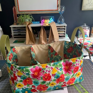May include: A floral fabric storage bin with three compartments and green handles. The bin is sitting on a gray cutting mat.
