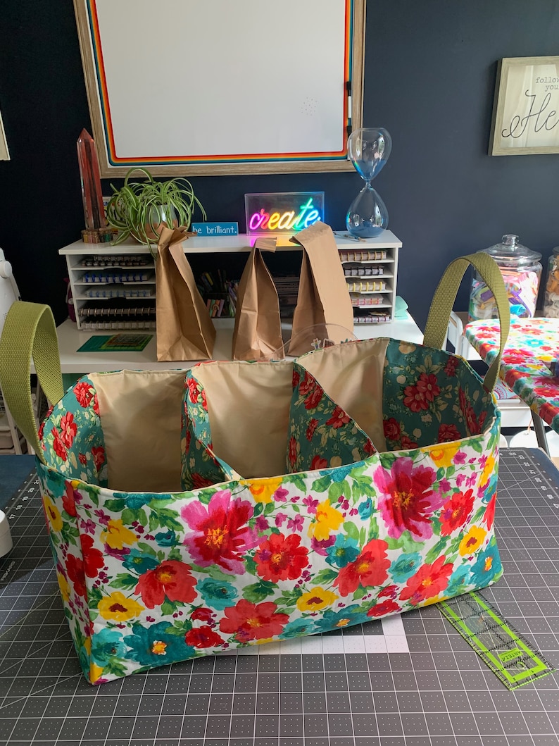 May include: A floral fabric storage bin with three compartments and green handles. The bin is sitting on a gray cutting mat.