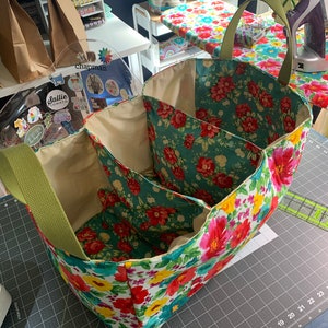 May include: A floral fabric storage bin with three compartments and green handles. The bin is sitting on a gray cutting mat with a ruler.