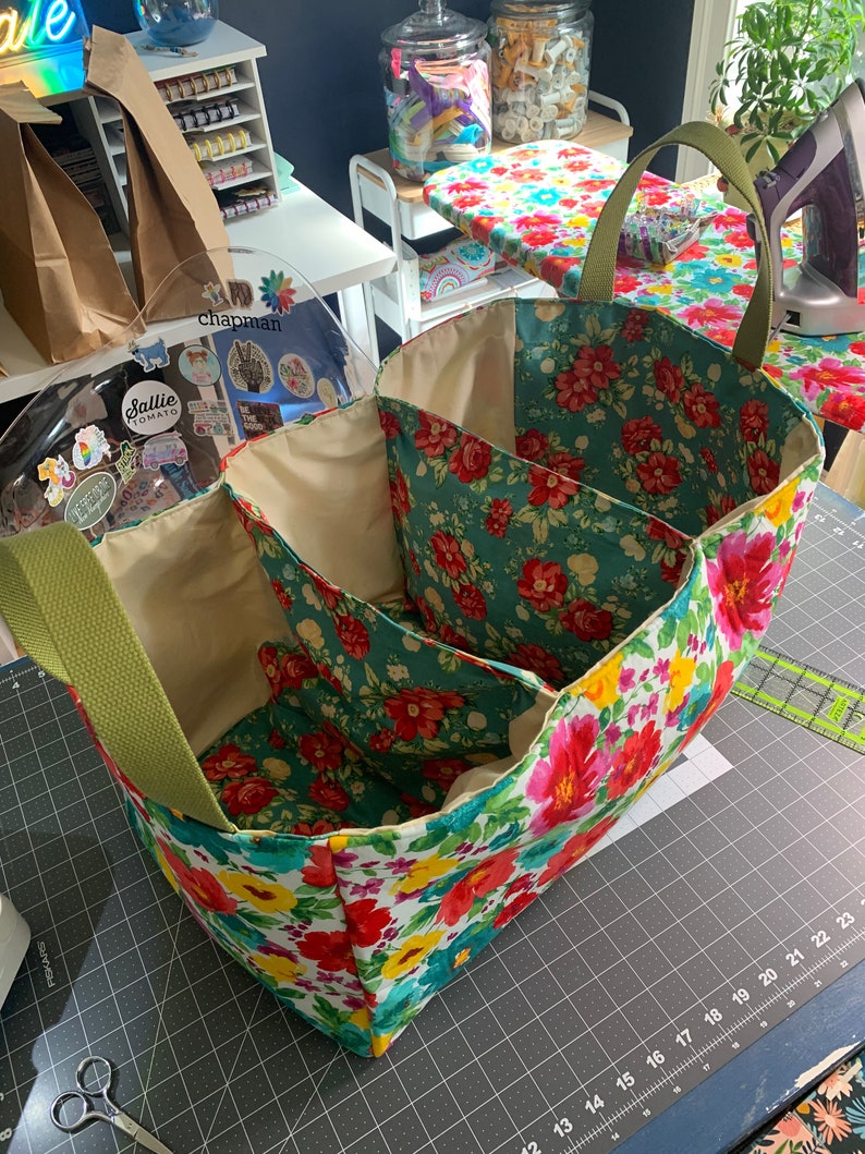 May include: A floral fabric storage bin with three compartments and green handles. The bin is sitting on a gray cutting mat with a ruler.