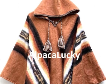 May include: A brown alpaca wool poncho with a hood and tassels. The poncho has a striped pattern in shades of brown, white, and black. The text "AlpacaLucky" is visible on the poncho.