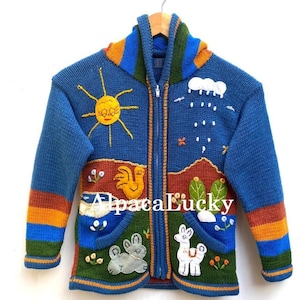Peut inclure: Un sweat à capuche en laine d'alpaga bleu avec une fermeture éclair. Le sweat est orné de détails brodés colorés représentant un soleil, des nuages, un coq, un lama et un lapin. Le texte "Alpaca Lucky" est brodé sur le devant du sweat.