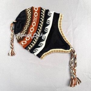 May include: A black and brown knitted hat with a geometric pattern and ear flaps. The hat has a long braided tassel.