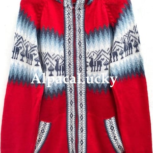 Puede incluir: Suéter rojo de lana de alpaca con capucha, cierre de cremallera y un patrón geométrico azul y blanco con llamas. El suéter tiene dos bolsillos en la parte delantera.