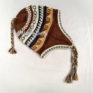 Könnte beinhalten: Braune Strickmütze mit geometrischem Muster und langen geflochtenen Quasten. Die Mütze hat eine Klappe, die über die Ohren gezogen werden kann.