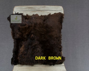 Op de afbeelding: Donkerbruin alpaca-vacht kussen. Het kussen ligt op een witte houten stoel.