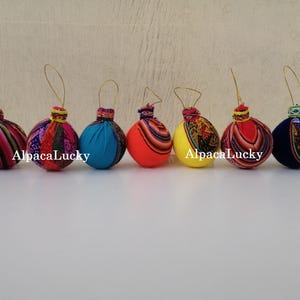 May include: A collection of six colorful, round ornaments. Each ornament features a fabric design with various patterns and colors, including red, blue, yellow, and patterned textiles. The text "AlpacaLucky" is visible on some of the ornaments.