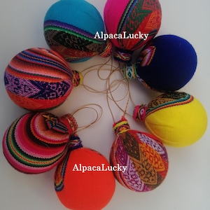 May include: A collection of colorful, round ornaments with patterned fabric accents. Each ornament has a different solid color, including blue, pink, orange, and yellow. The text "AlpacaLucky" is visible on some of the ornaments.