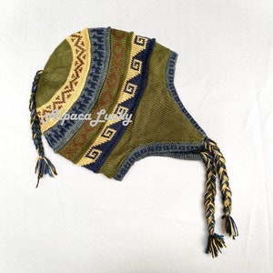 Könnte beinhalten: Eine grüne Strickmütze mit geometrischem Muster und zwei langen Zöpfen. Die Mütze hat eine umklappbare Klappe, die die Ohren bedeckt.