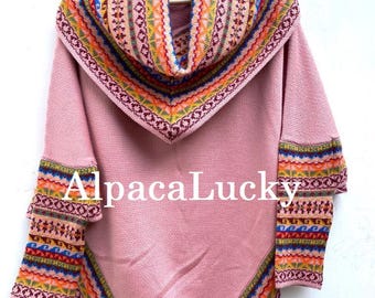Può includere: Un poncho in lana di alpaca rosa con un motivo geometrico colorato attorno al collo e all'orlo. Il poncho ha un collo alto e maniche lunghe. Il testo "AlpacaLucky" è visibile sul davanti del poncho.