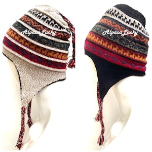May include: Two alpaca wool knit hats with ear flaps and tassels. The hats have a geometric pattern in red, black, white, and brown. The text "Alpaca Lucky" is printed on each hat.
