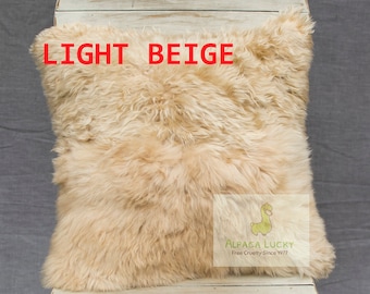 Op de afbeelding: Licht beige schapenvacht kussen met de tekst "ALPACA LUCKY Free Cruelty Since 1977" in de rechter benedenhoek.