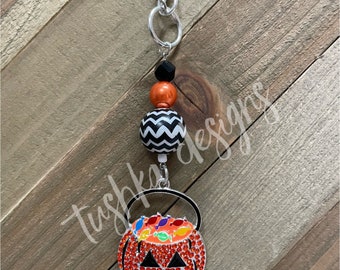 Op de afbeelding: Een zilveren ketting met een zwart-witte chevron-kraal, een oranje kraal en een zwarte kraal. De ketting eindigt met een zilveren bedel in de vorm van een pompoen met een gezicht en snoep erin.