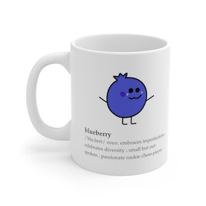 May include: White ceramic mug with a cartoon blueberry illustration and the definition of the word "blueberry". The definition reads:  /'blu beri/ noun. embraces imperfections. celebrates diversity; small but outspoken; passionate rookie chess-player.
