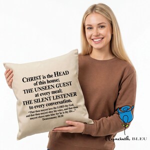May include: A beige square cushion with black text that reads "CHRIST is the HEAD of this house; THE UNSEEN GUEST at every meal; THE SILENT LISTENER to every conversation." The cushion is held by a person.