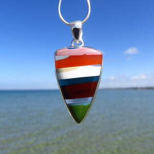 May include: A silver pendant with a multi-colored, layered, teardrop-shaped stone. The stone is red, orange, white, blue, green, and brown.