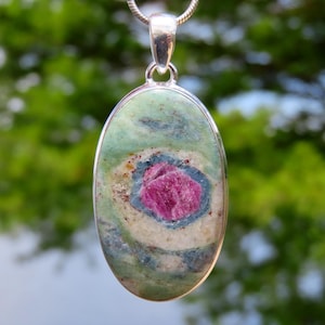 May include: Oval pendant with a silver bail and chain. The pendant features a colourful stone with a pink centre, surrounded by blue, green, and white swirls. The stone is set in a silver bezel.