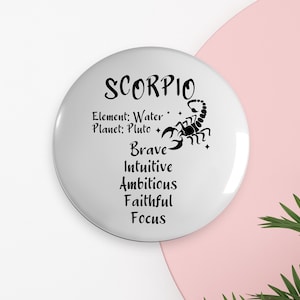 May include: White round button with black text and a scorpion graphic. The text reads "Scorpio", "Element: Water", "Planet: Pluto", "Brave", "Intuitive", "Ambitious", "Faithful", "Focus".
