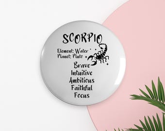 Puede incluir: Botón redondo blanco con texto negro y un gráfico de escorpión. El texto dice "Scorpio", "Elemento: Agua", "Planeta: Plutón", "Valiente", "Intuitivo", "Ambicioso", "Fiel", "Enfoque".