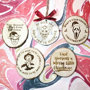 May include: Five round wooden ornaments with gold text and images. The ornaments feature quotes from popular horror movies, including "Have Yourself a Gary Little Christmas", "He Sees You When You're Sleeping", "What's Your Favorite Christmas Movie?", "Hail Yourself a Merry Little Christmas", and "He Knows When You're Awake".