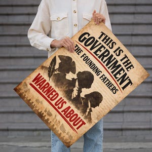 Może przedstawiać: Plakat w stylu vintage z napisem "THIS IS THE GOVERNMENT THE FOUNDING FATHERS WARNED US ABOUT." Plakat przedstawia sylwetki postaci i pi&oacute;ro, z postarzanym, zużytym wyglądem. Plakat jest trzymany przez osobę.