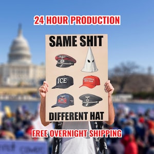 May include: A person holding a sign with the text "24 HOUR PRODUCTION" and "SAME SHIT DIFFERENT HAT." The sign displays images of various hats, including a red and black military cap, a white hood, and baseball caps.